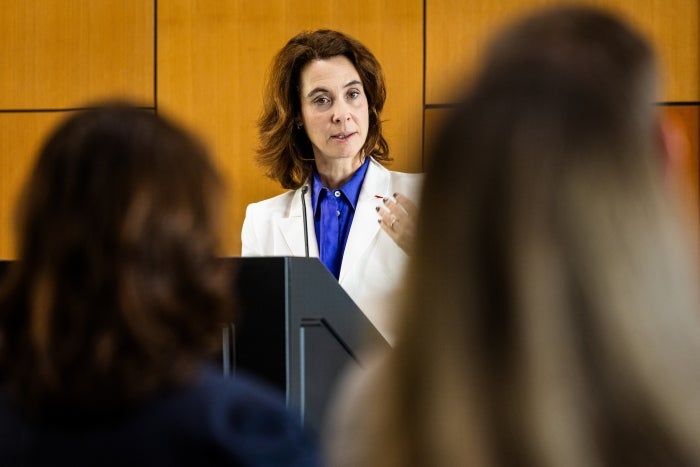 Woman with medium brown hair wearing a white blazer speaks to audience behind a lectern