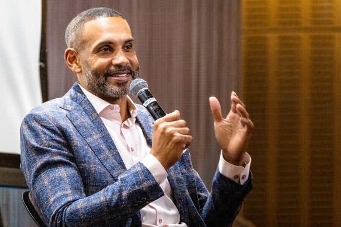 ASU basketball Hall of Famer Grant Hill, wearing a blue plaid sports coat speaks into a microphone