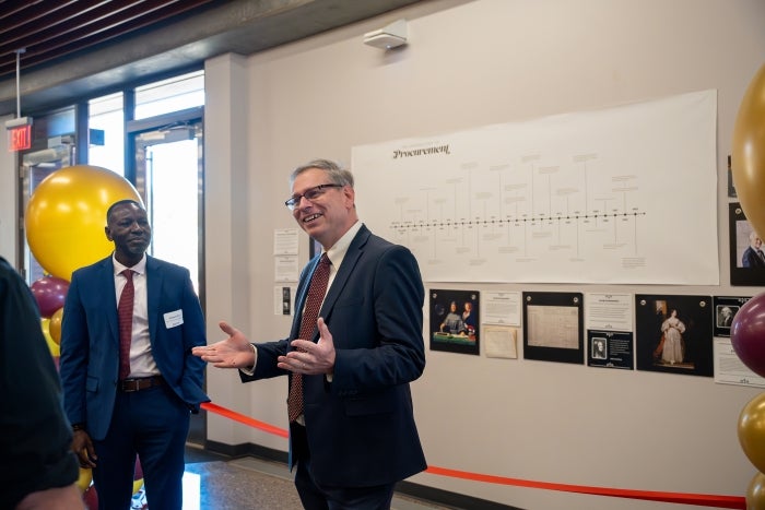 Two people chat and smile in front of exhibit timeline on wall.