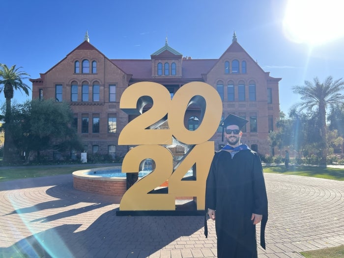 Person in graduation attire standing in front of a large "2024" sculpture.