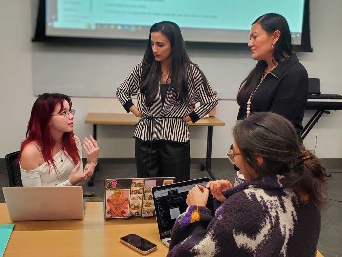 Two women speaking to students seated at a table.