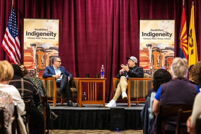 Two people sitting on stage talking while audience listens