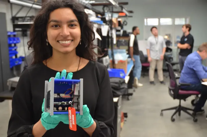 A student poses with a CubeSat model