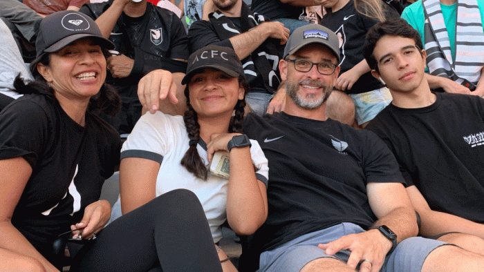 Two parents and two teens pose for a photo in the bleachers at a game