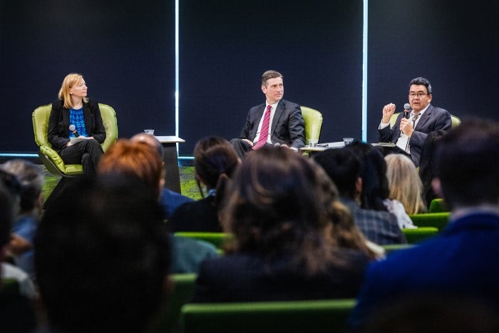 A woman and 2 men sit in the front of a large room