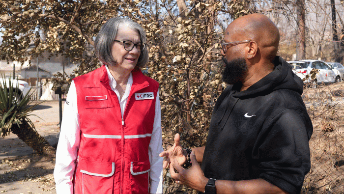 A woman in a Red Cross vest speaks with a man outside