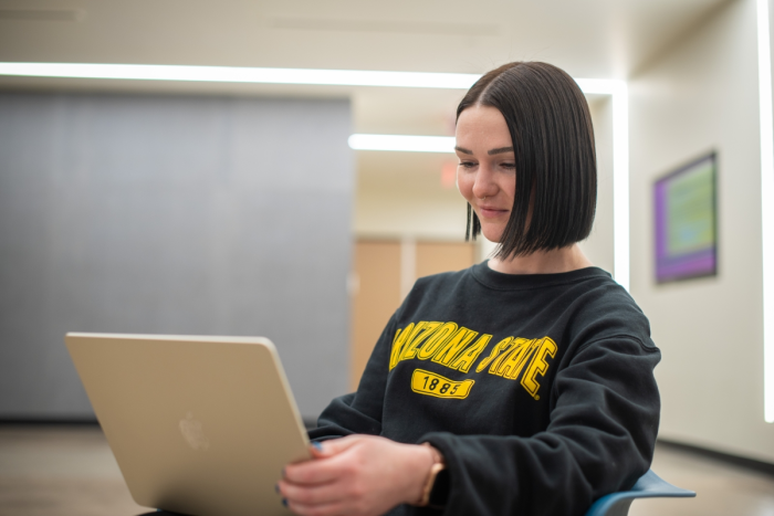 A dark-haired woman wearing an ASU sweatshirt works at a laptop. Photo by Mike Sanchez/ASU ET.