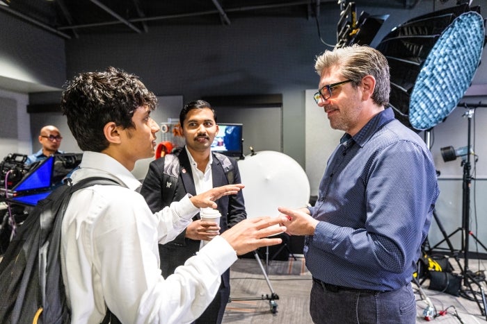 A man speaks with two students in a video studio