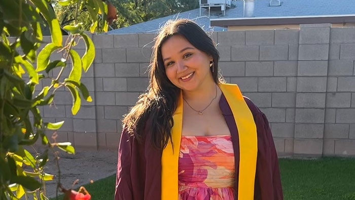 Portrait of graduate in maroon gown in backyard