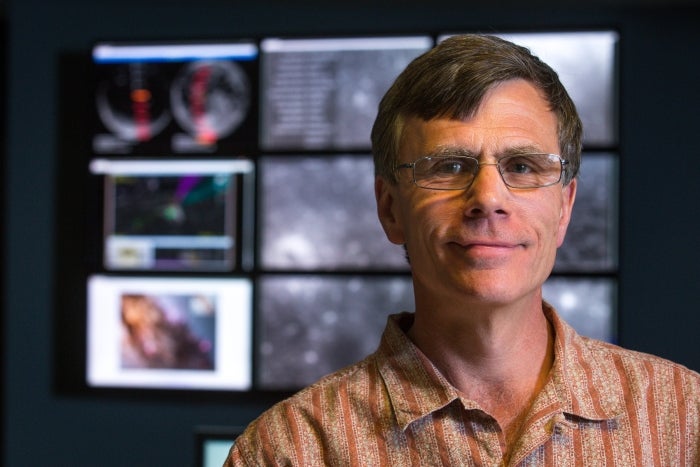 A man stands in front of monitors showing moon images.