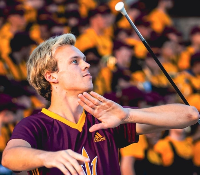 ASU graduating student twirling baton for ASU. Foreground is Cody with baton in action, background is blurred shot of audience in stadium