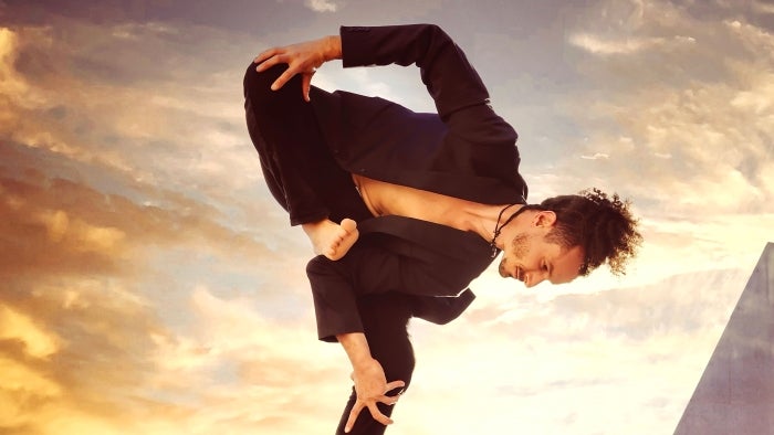 Man posing in a a standing balance position in front of a sky at dusk.