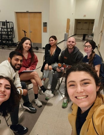 Students sit in chairs planning and smiling at the camera