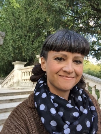 Adrienne Keller takes a selfie outside with green trees and a white marble staircase behind her​