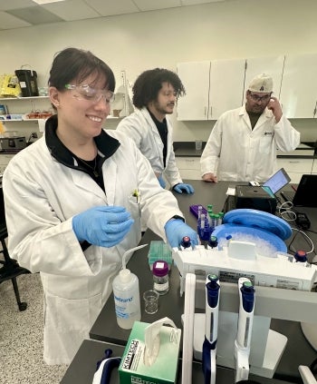 Three people in lab gear working in a lab