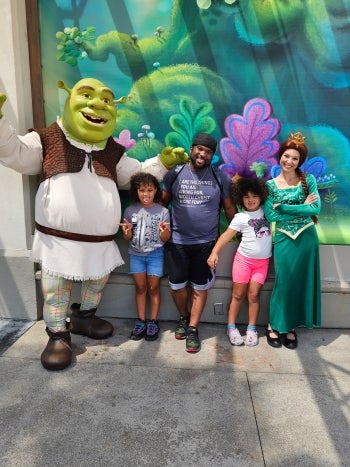 Man and his two children stand with Shrek and Princess Fiona at a theme park.