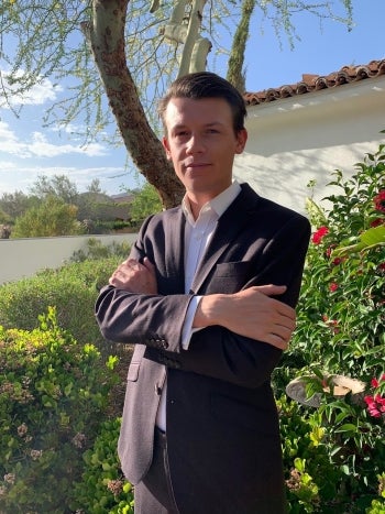 Man in dark blazer poses in front of a tree