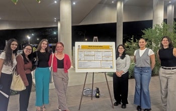 Seven women stand around a research poster.