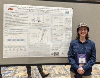 A woman in a blue shirt and a bucket hat standing in front of a research poster