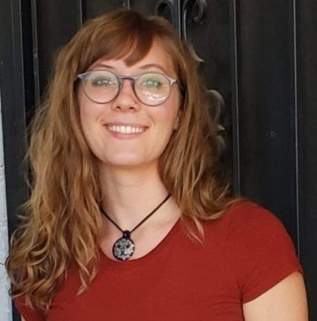 A woman with blonde hair, glasses, a pendant necklace and a red shirt smiling at the camera.