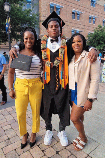 A man in graduation regalia stands with his arm around two women