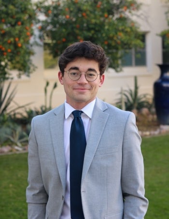 ASU student Collin Frank pictured standing and looking at camera in an outdoor setting, dressed in a suit and tie.