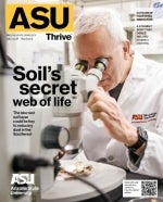 A man wearing an ASU Biodesign Institute lab coat while looking through a microscope