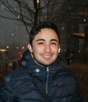 A smiling man wearing a zipped up jacket in the snow.