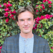 A blonde man standing in front of a bouganvillea bush.