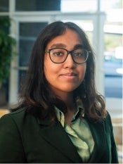 Portrait of young woman with long dark hair and glasses wearing a green blouse and black blazer