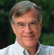 Portrait of a man with light brown hair wearing glasses and a white and blue striped button down shirt