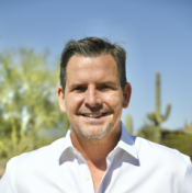 Portrait of white male with short brown hair wearing a white button down shirt in front of a desert background