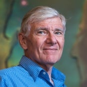 Portrait of an older man with white hair a white and blue striped button down shirt in front of a Hubble image