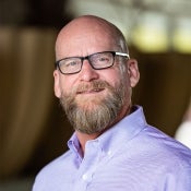 Associate Dean and Professor David W. Coon pictured in a professional portrait. He is waring a lavender button up shirt and glasses.