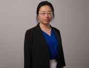 Professor Fang Yu pictured in a professional portrait. She is wearing a black blazer with a blue button up shirt.