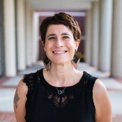 Courtesy photo of new faculty member Angela Rounsaville, who wears a black top and dramatic earrings while standing in a  colonnade.