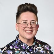 ASU directory photo of new faculty Jed Samer, who smiles while wearing glasses and sporting a colorful button-up top.