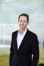 Photo of Matthew Scott in black jacket standing in front of a fence