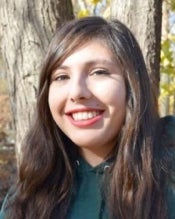 Portrait of a young woman with long brown hair outside in front of a tree