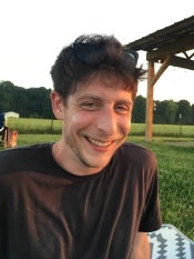 A man smiles in front of a grassy field.