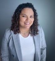 Katherine Bynum, ASU Online assistant professor in the School of Historical, Philosophical and Religious Studies, smiles into the camera. She has dark, curly hair just past her shoulders and is wearing a choker-length necklace, white shirt and light-plaid patterned blazer. 