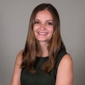 A brunette woman smiles at the camera with a grey backdrop.