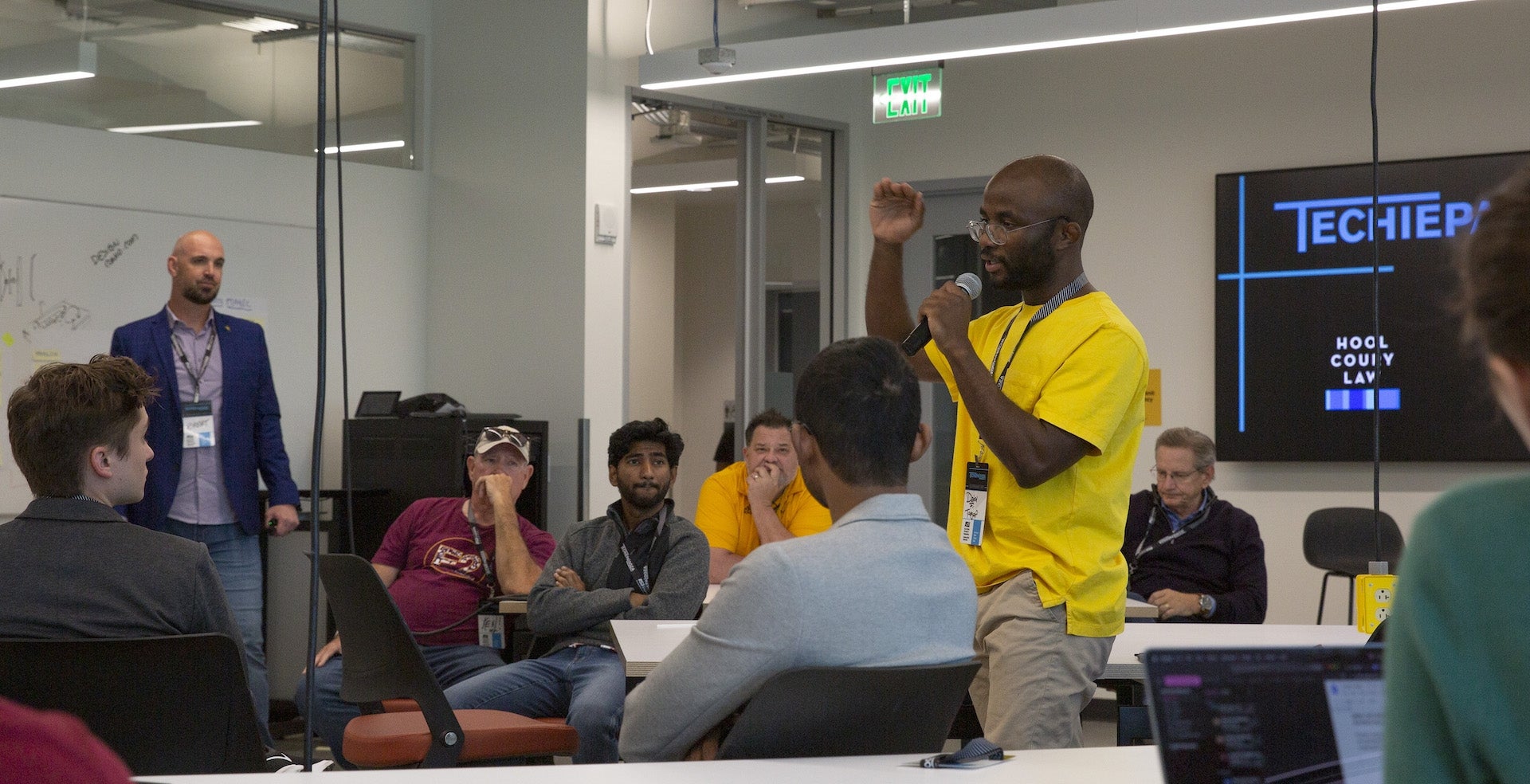 Man speaking into a microphone in a room full of people.