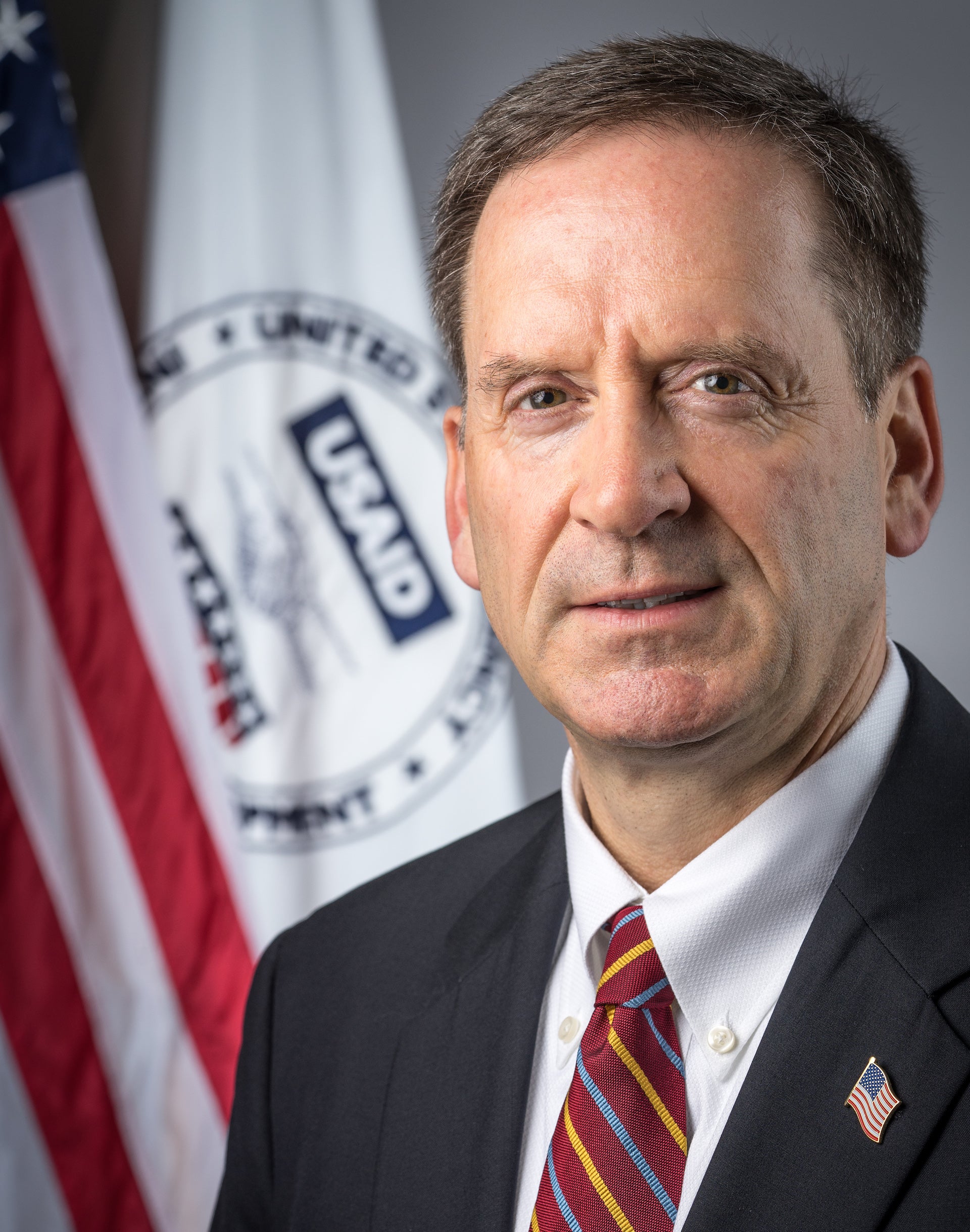 Man in suit and tie with flag behind him