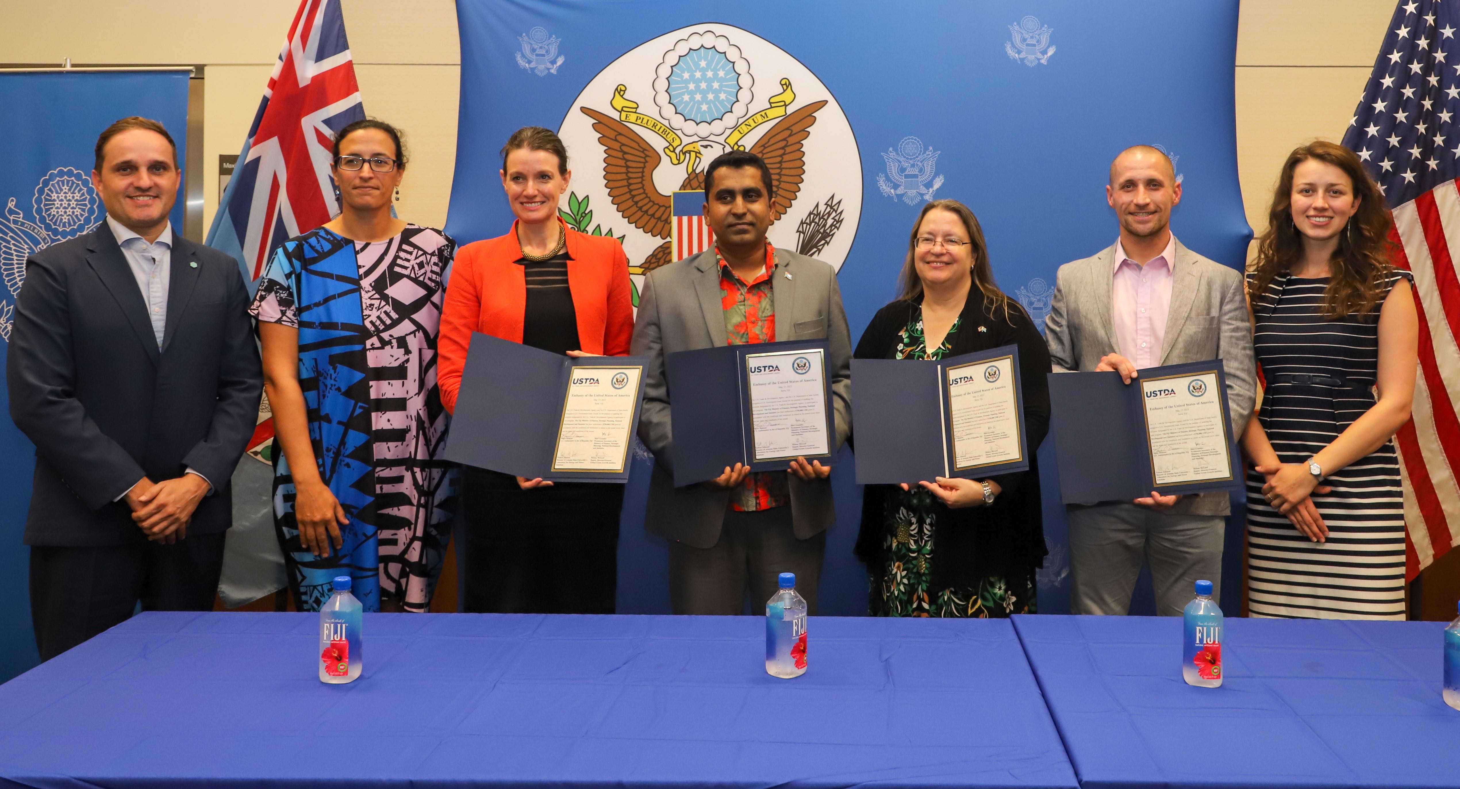 A group photo of people holding signed paperwork in front of an official seal