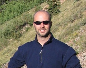 headshot of a man wearing sunglasses and a dark blue shirt with nature in the background