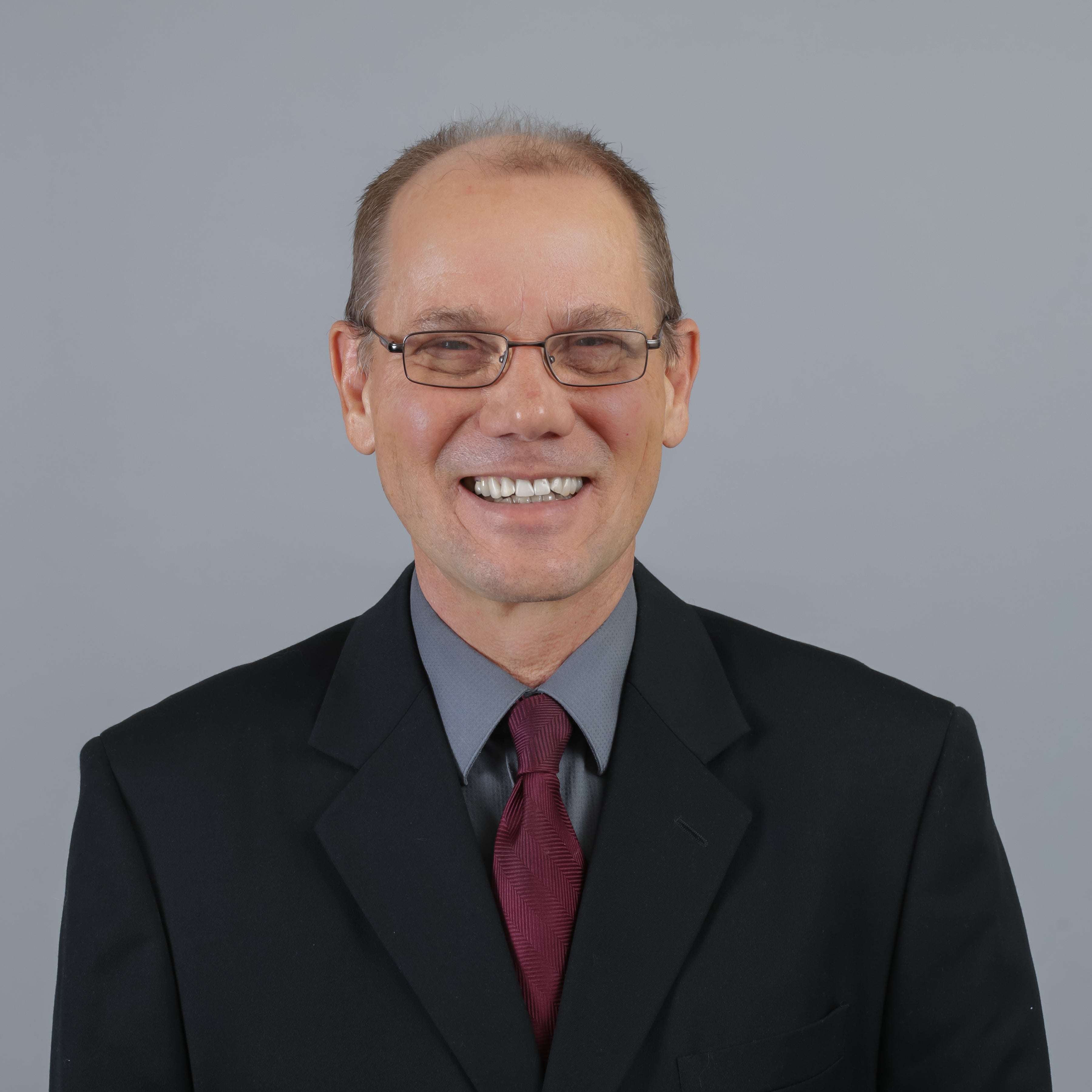 Man in dark suit and glasses smiling