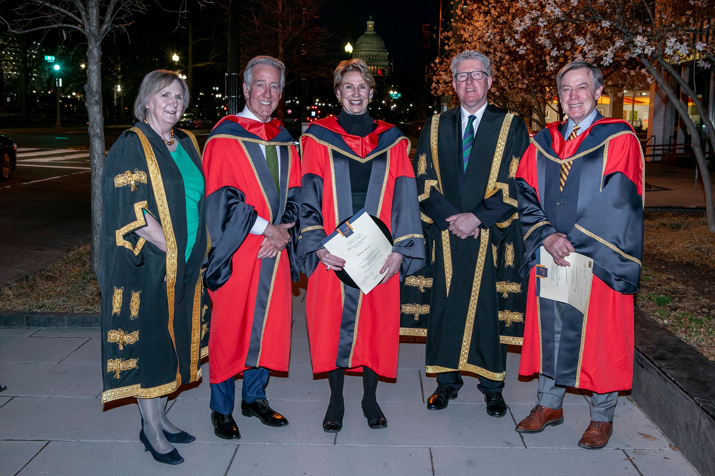 Five people in ceremonial commencement gowns pose for a photo outside